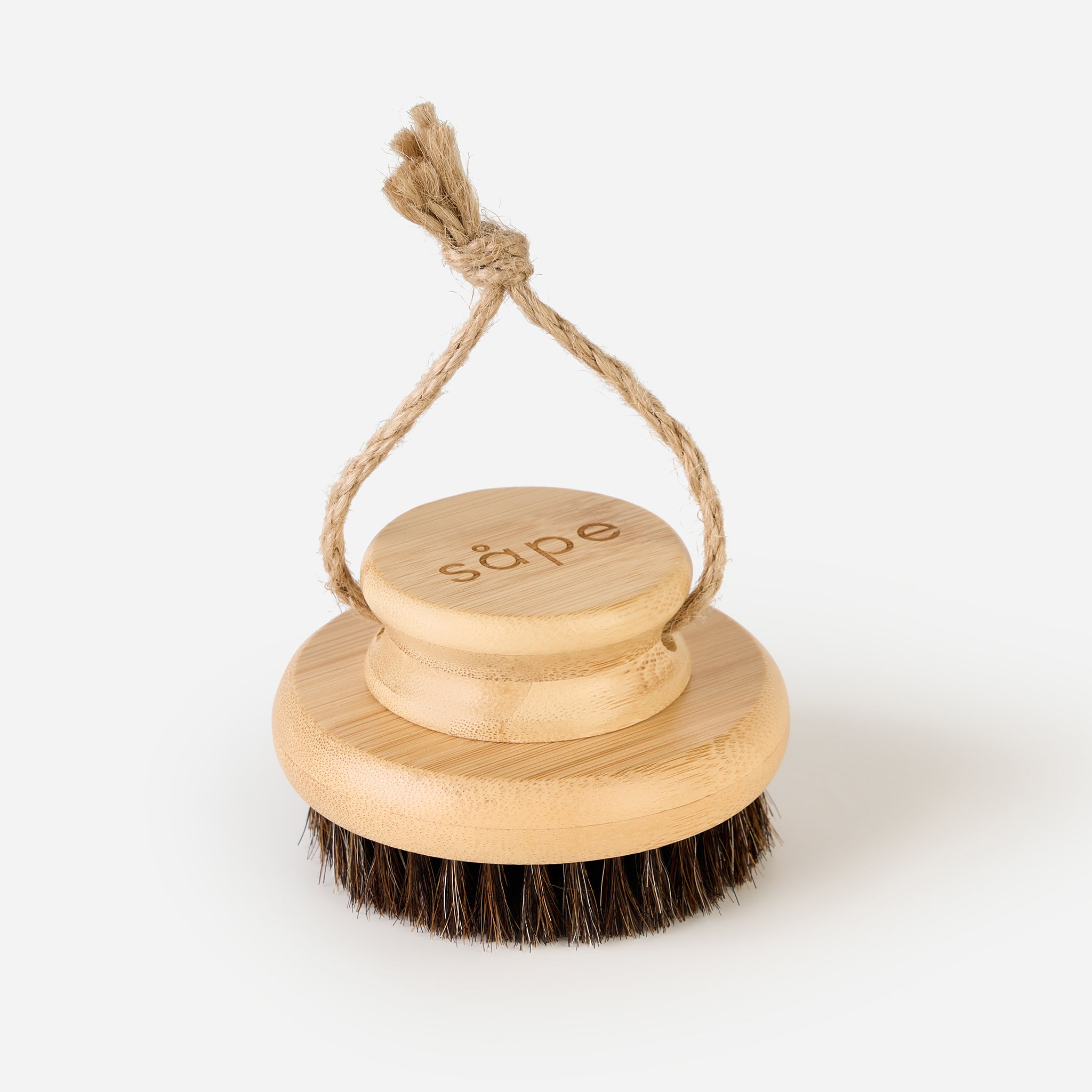 Angled view of Horsehair Body Brush hanging by natural rope against a white background