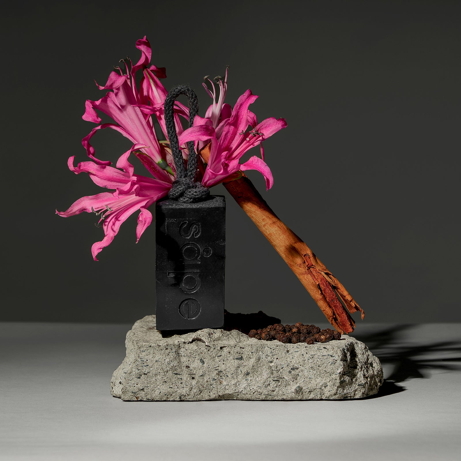 Black Myrk soap with pink flowers and cinnamon sticks, styled on natural stone