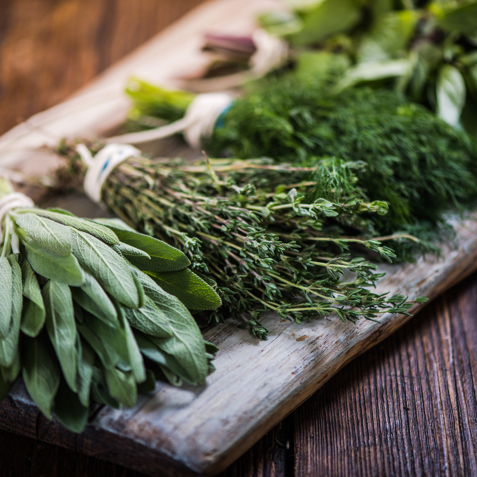 Overhead view of assorted fresh botanicals on a wooden board including rosemary, sage, and lavender