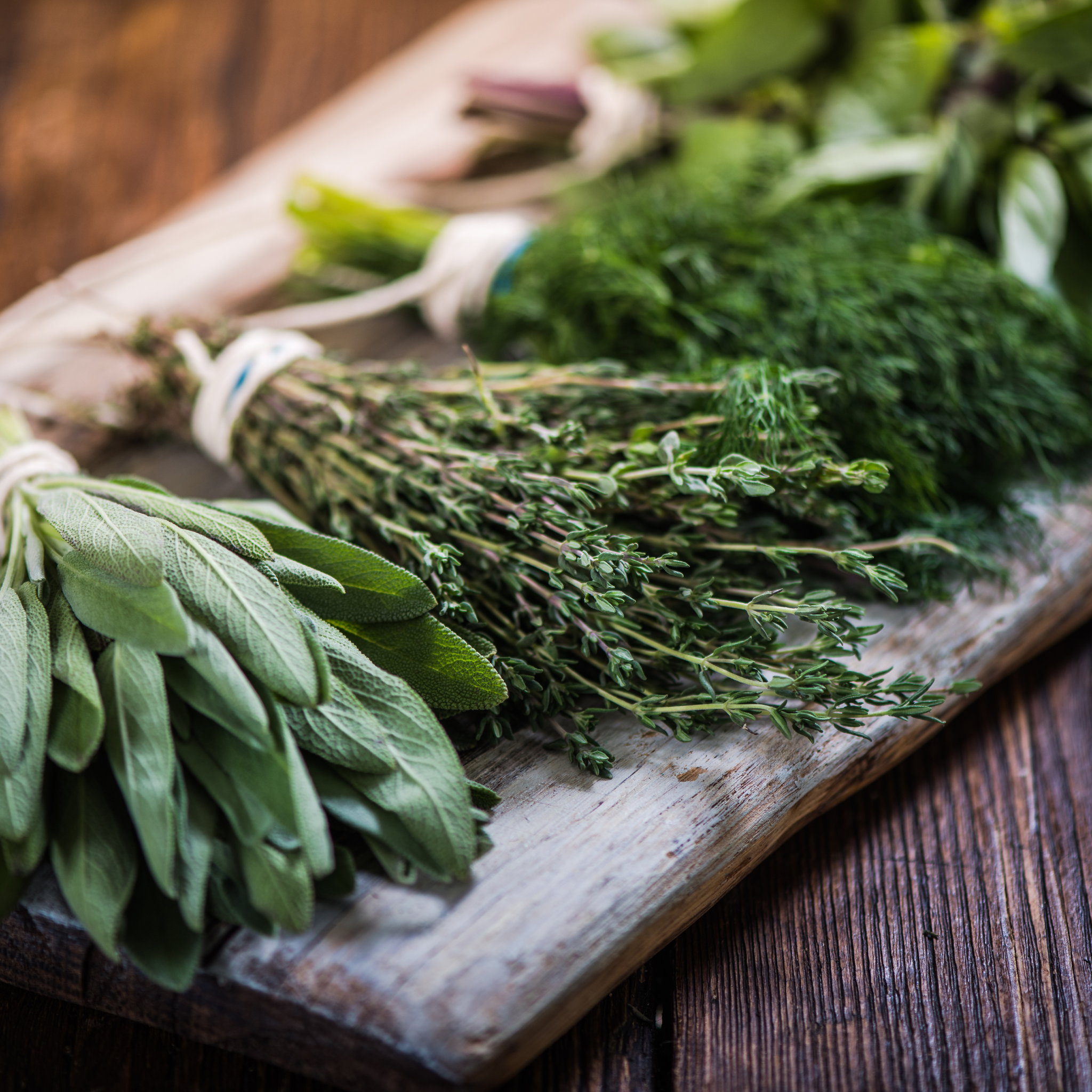 Overhead view of assorted fresh botanicals on a wooden board including rosemary, sage, and lavender